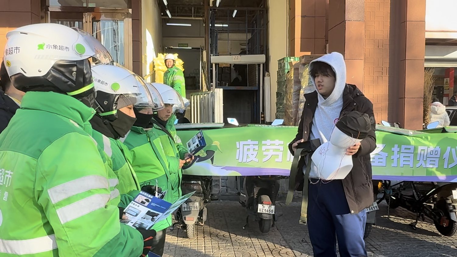 A rider in a white helmet receives the fatigue detection device while the team member explains the equipment.