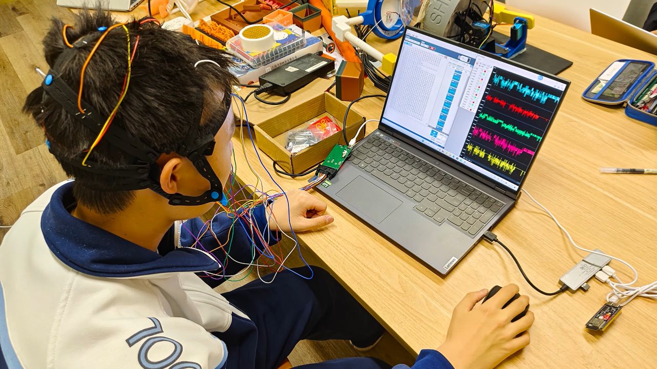 A test session: the helmet fitted with electrode wiring while a laptop displays live EEG waveforms.